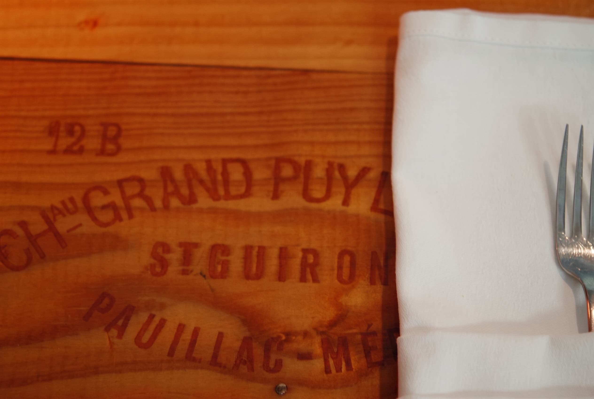 A napkin and fork set on a Chateau Grand-Puy Pauillac wine crate table top